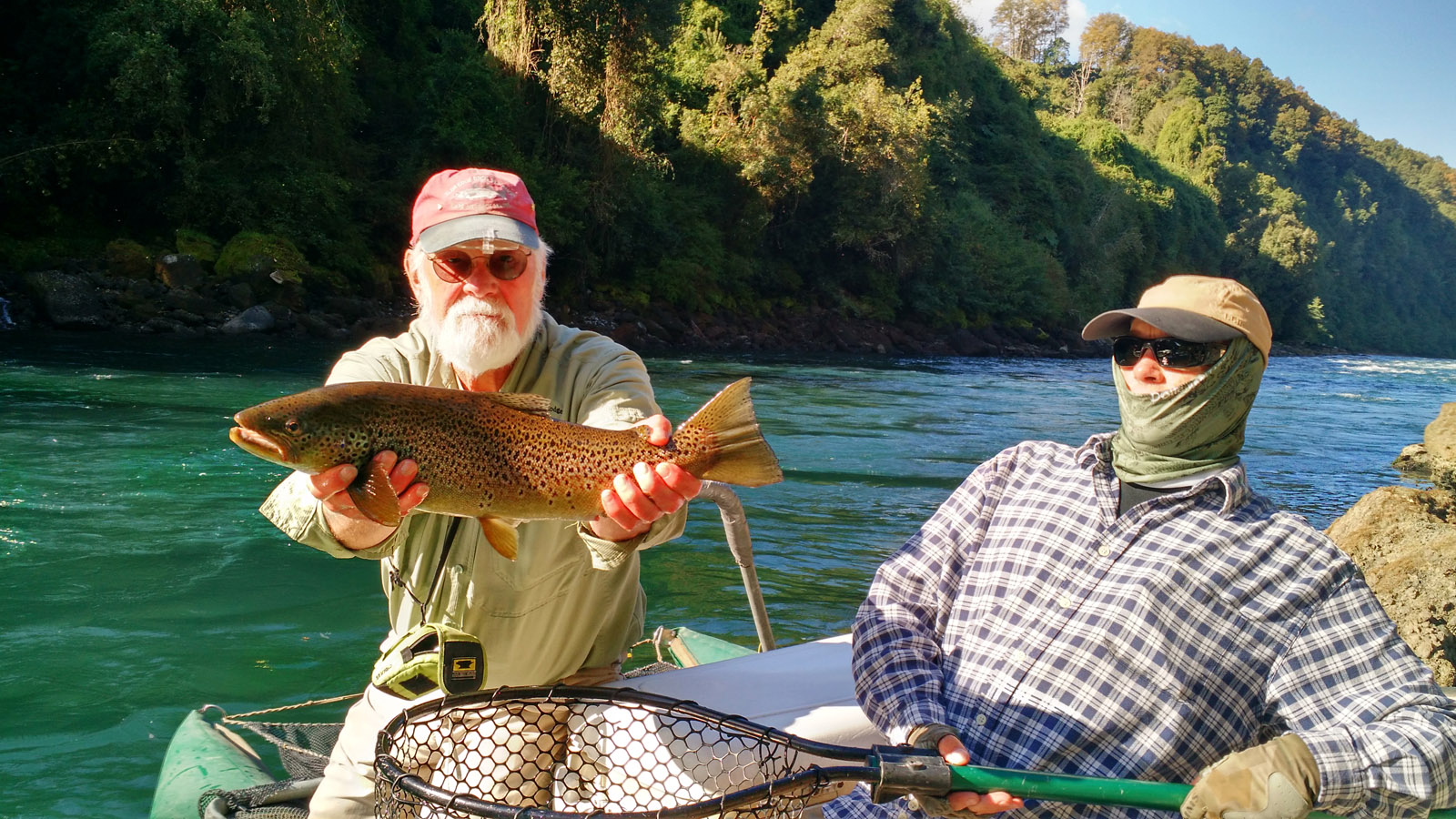 The fishing guide looks on as Rick holds up a nice brown trout that he caught on a float trip on the Pilmaiquen river that flows from lago Puyehue in Patagonia Chile, Lakes Region.